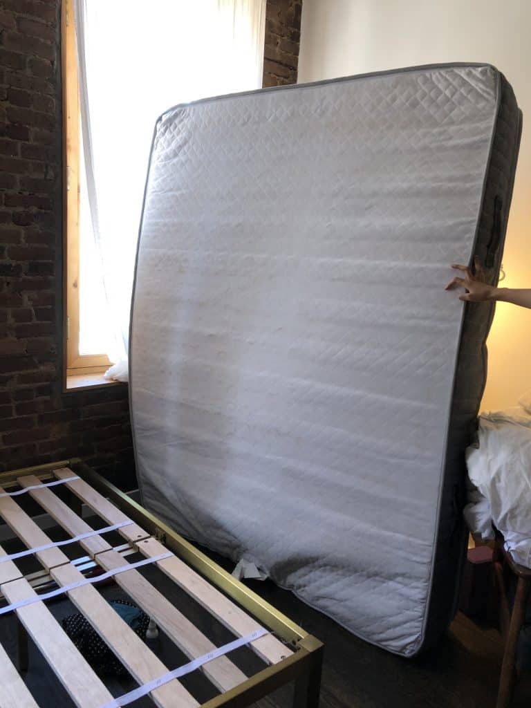 mattress and bed frame. The mattress is standing up getting ready for the bed bug cover to be slipped on.
